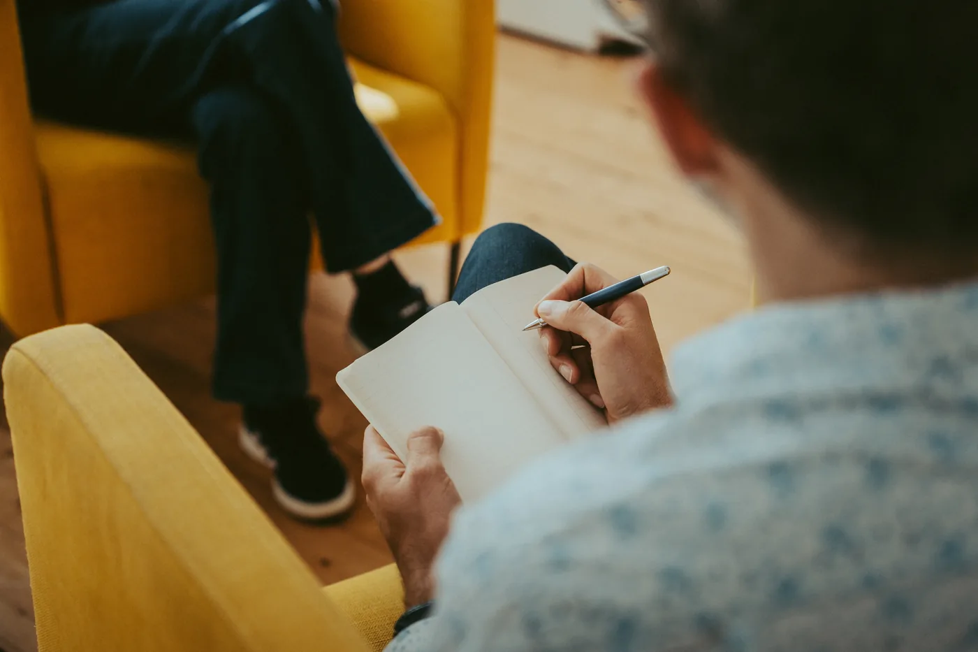 Deux fauteuils face à face, une personne prend des notes dans un carnet pendant un entretien